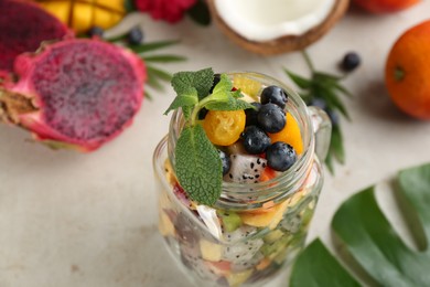 Photo of Delicious exotic fruit salad in mason jar on light grey table