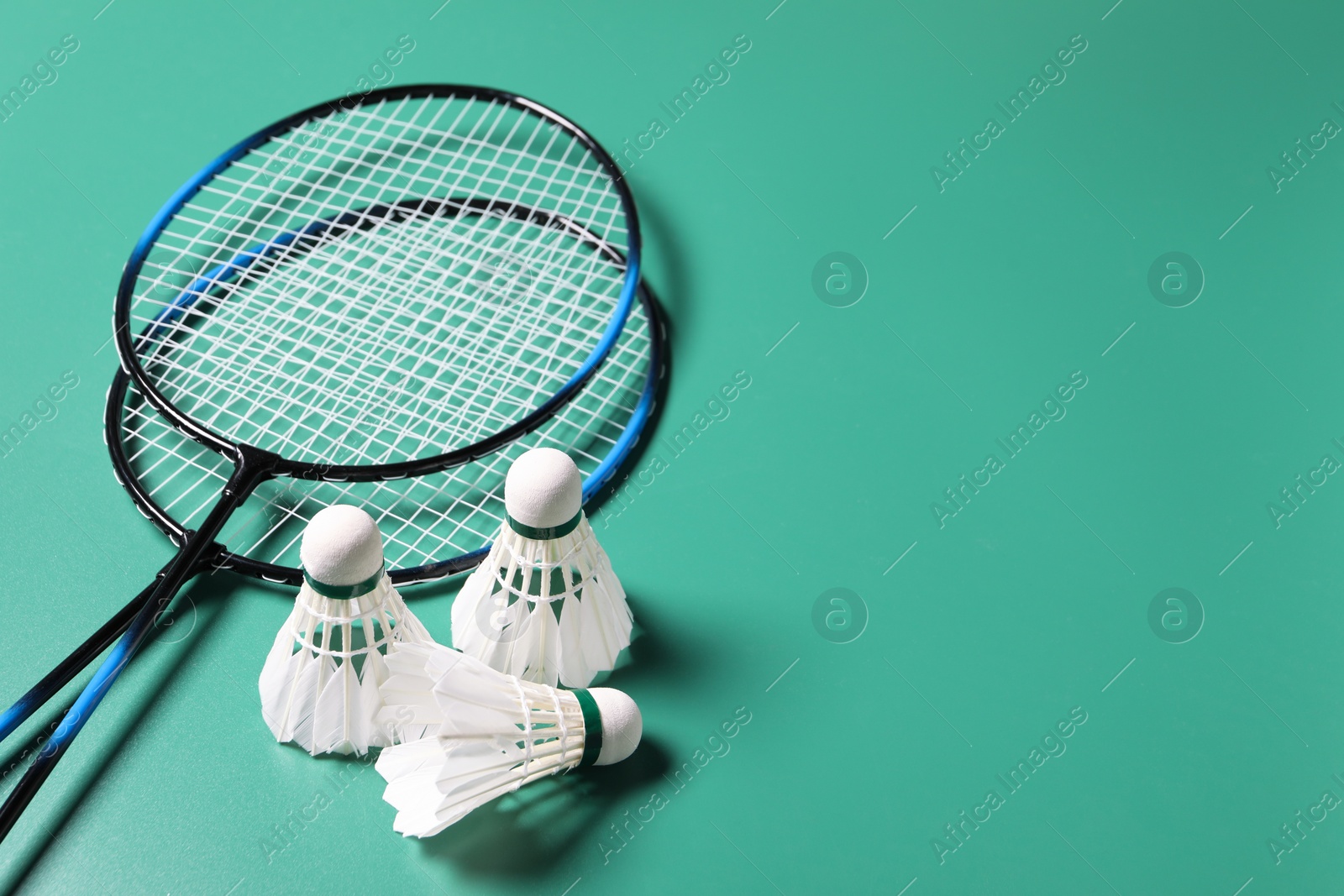 Photo of Feather badminton shuttlecocks and rackets on green background. Space for text