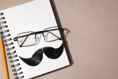 Flat lay composition with artificial moustache and glasses on light brown background, space for text
