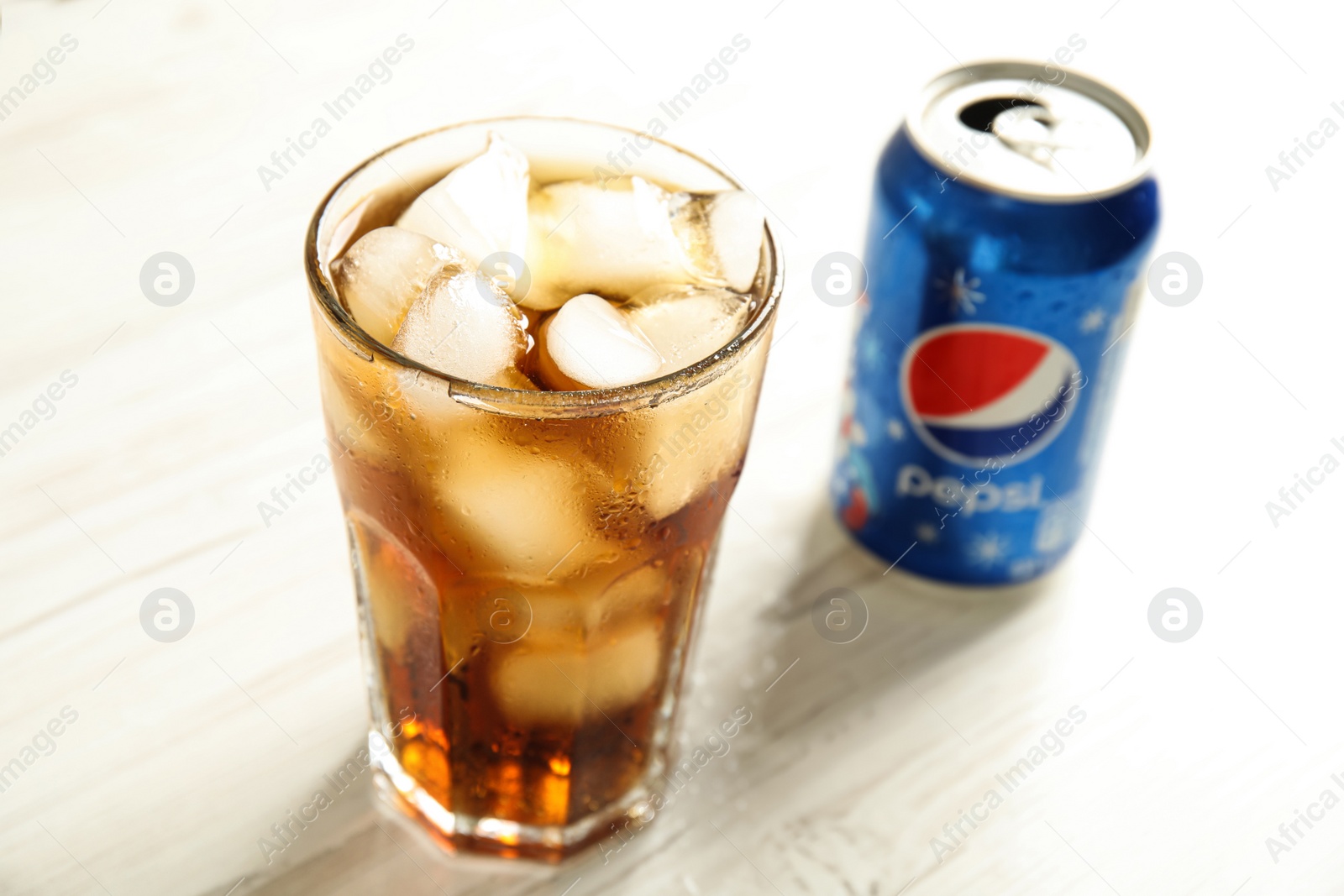 Photo of MYKOLAIV, UKRAINE - FEBRUARY 10, 2021: Glass and can of Pepsi on white wooden table