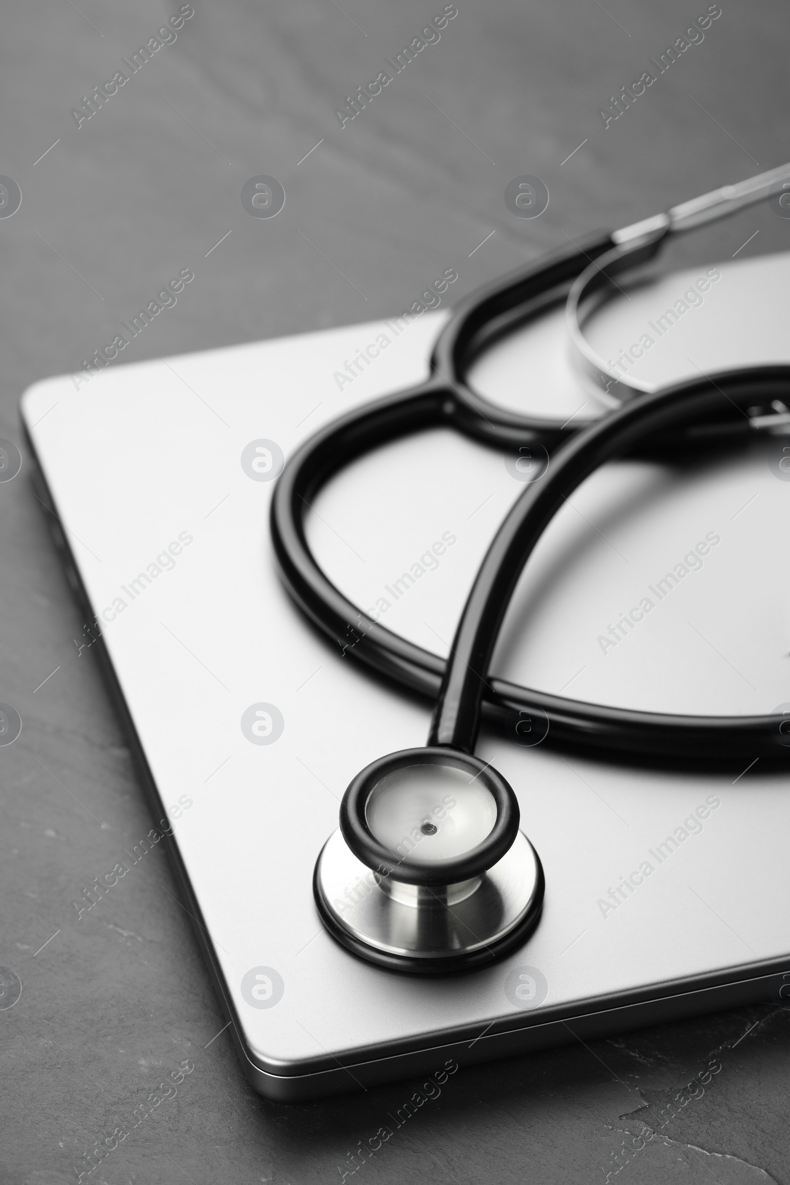 Photo of Modern laptop and stethoscope on black table, closeup