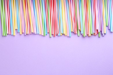 Colorful plastic drinking straws on violet background, flat lay. Space for text