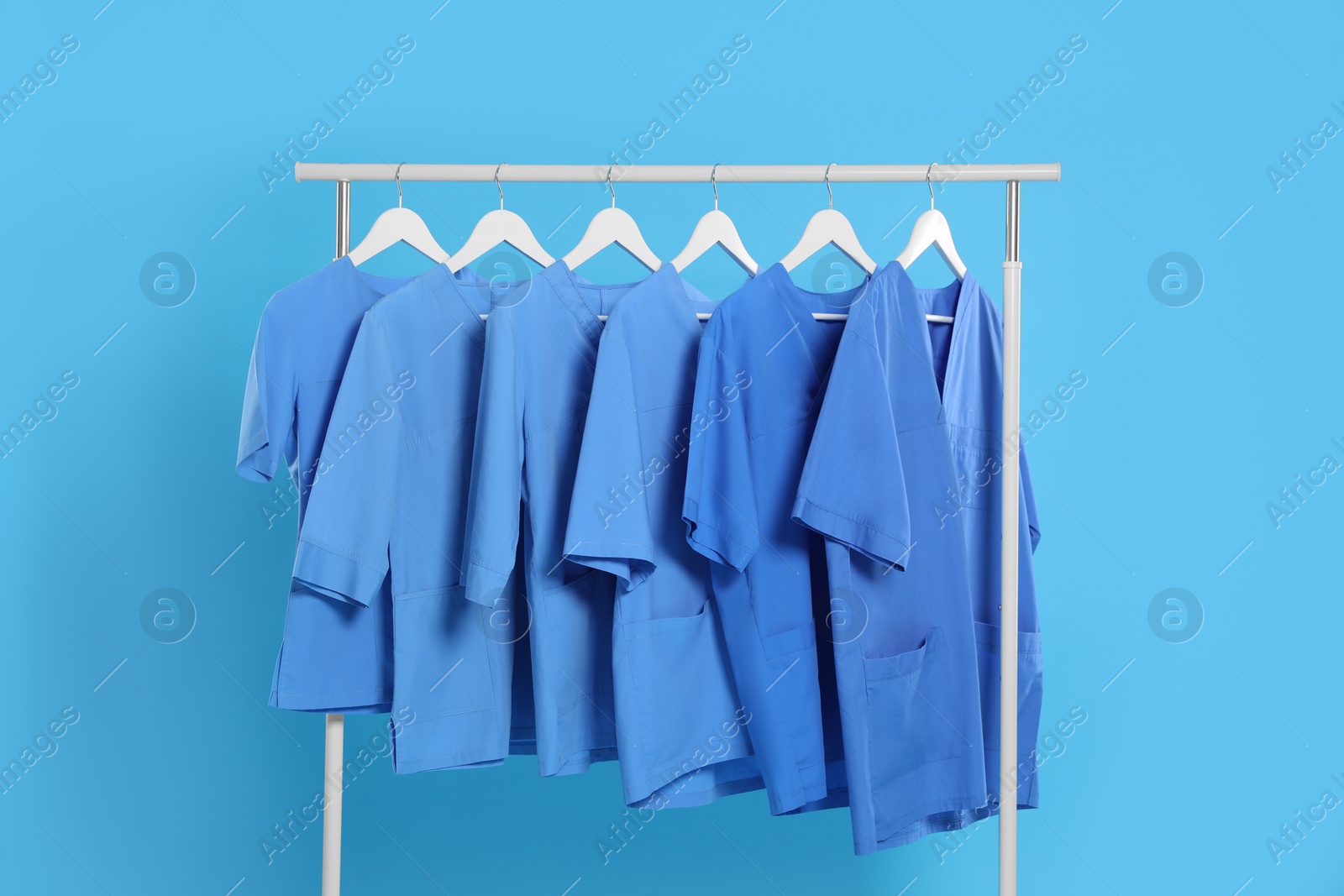 Photo of Medical uniforms on rack against light blue background