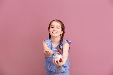 Cute girl eating tasty yogurt on color background