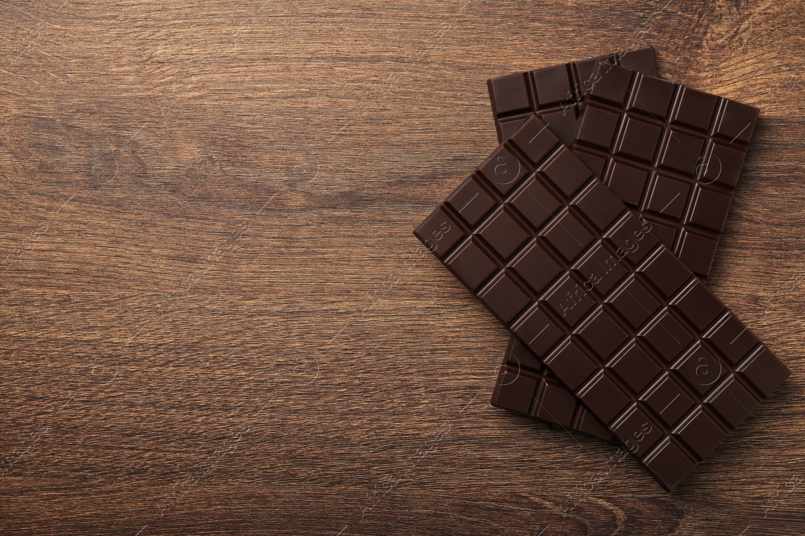 Photo of Tasty chocolate bars on wooden table, flat lay. Space for text