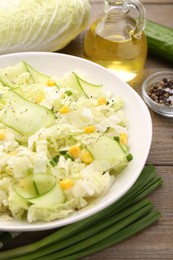 Tasty salad with Chinese cabbage in bowl and ingredients on wooden table, closeup