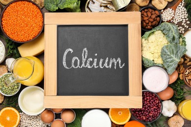 Photo of Set of natural food and chalkboard with written word Calcium on wooden table, flat lay