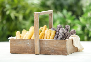 Photo of Different raw carrots in wooden basket on white table against blurred background