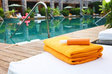 Beach towels and sunscreen on sun lounger near outdoor swimming pool. Luxury resort