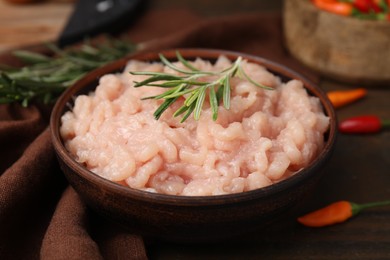 Fresh raw minced meat and rosemary in bowl on wooden table, closeup