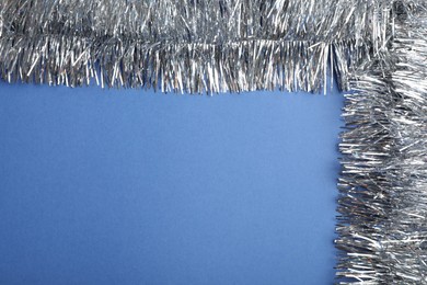 Photo of Silver tinsel on blue background, top view. Space for text