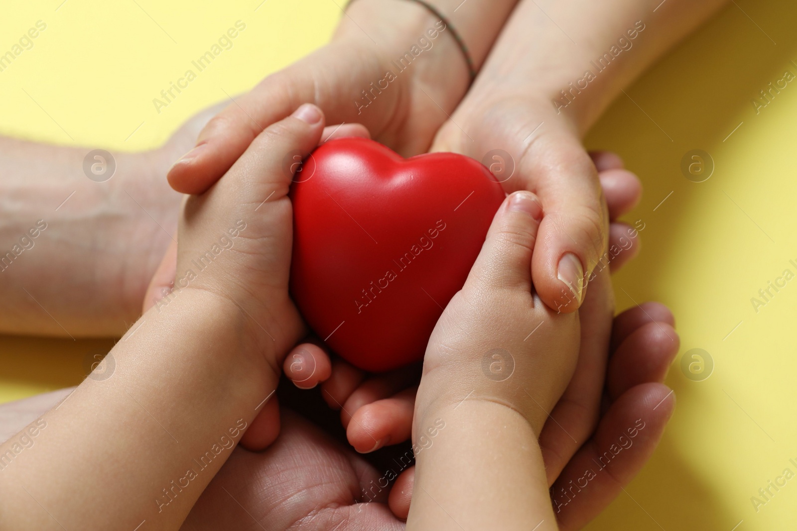 Photo of Parents and child holding red decorative heart on pale yellow background, closeup