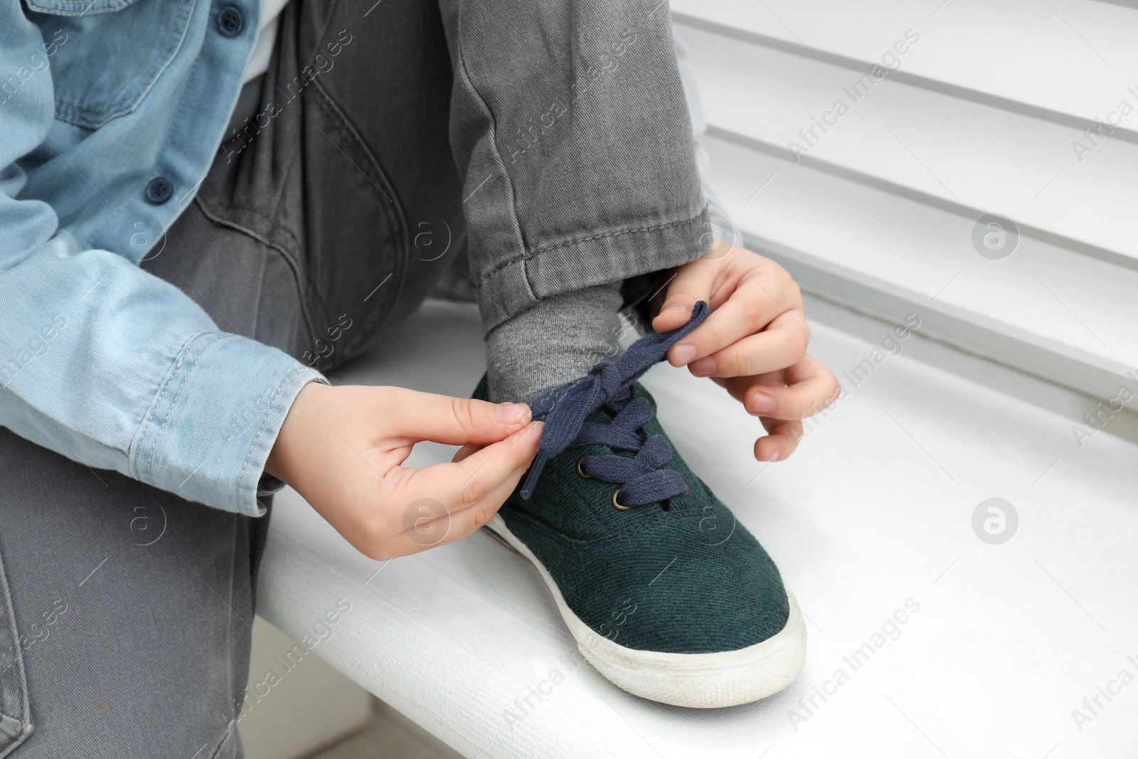 Photo of Little boy tying shoe laces at home, closeup