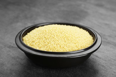 Photo of Bowl of raw couscous on grey table, closeup