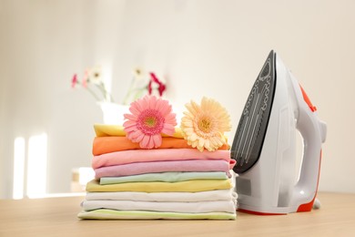 Photo of Stack of clean clothes, modern iron and flowers on wooden table