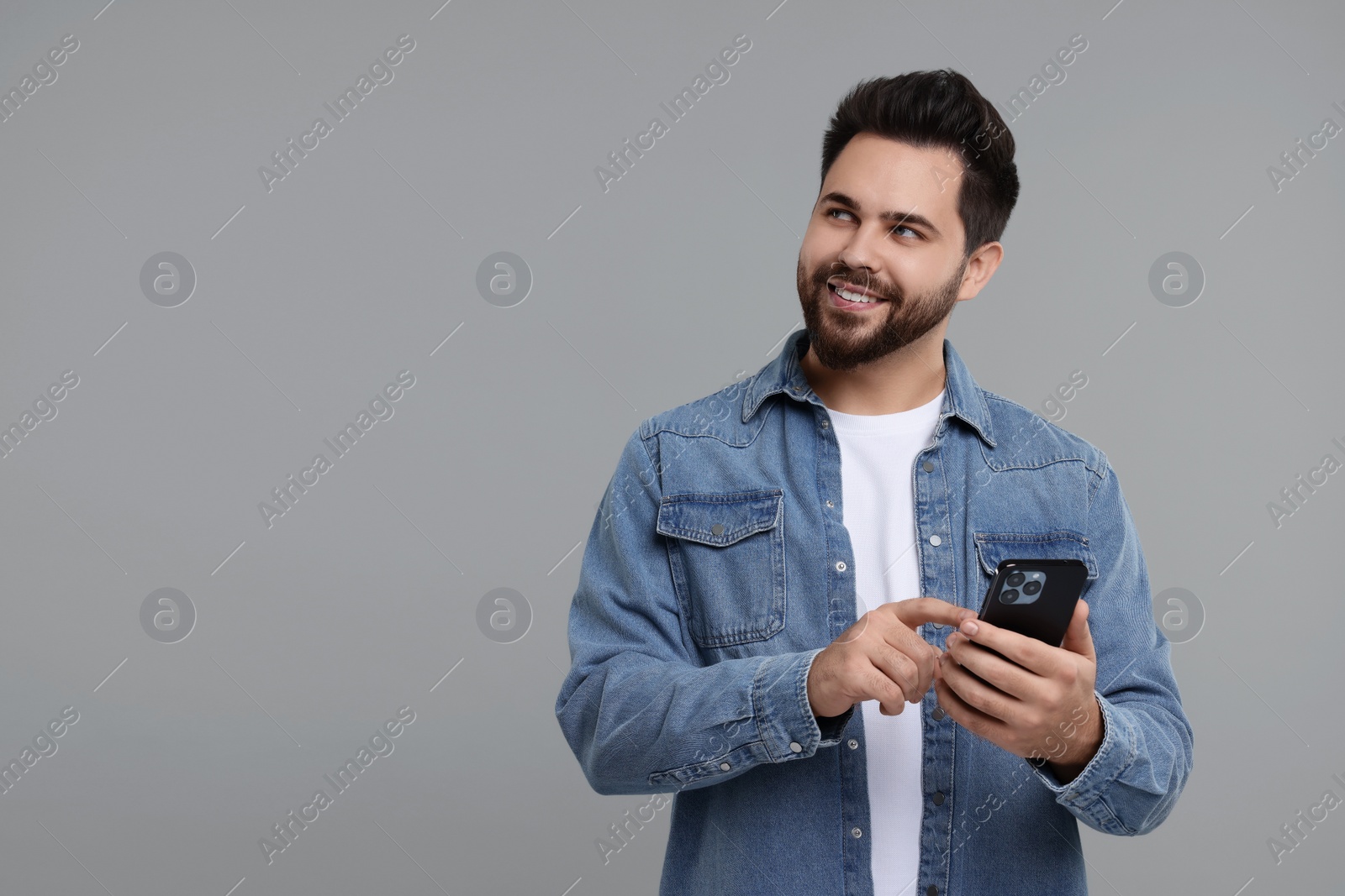 Photo of Happy young man using smartphone on grey background, space for text