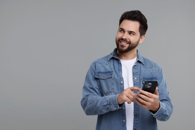 Happy young man using smartphone on grey background, space for text