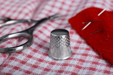 Photo of Silver thimble on checkered cloth, closeup. Sewing accessory