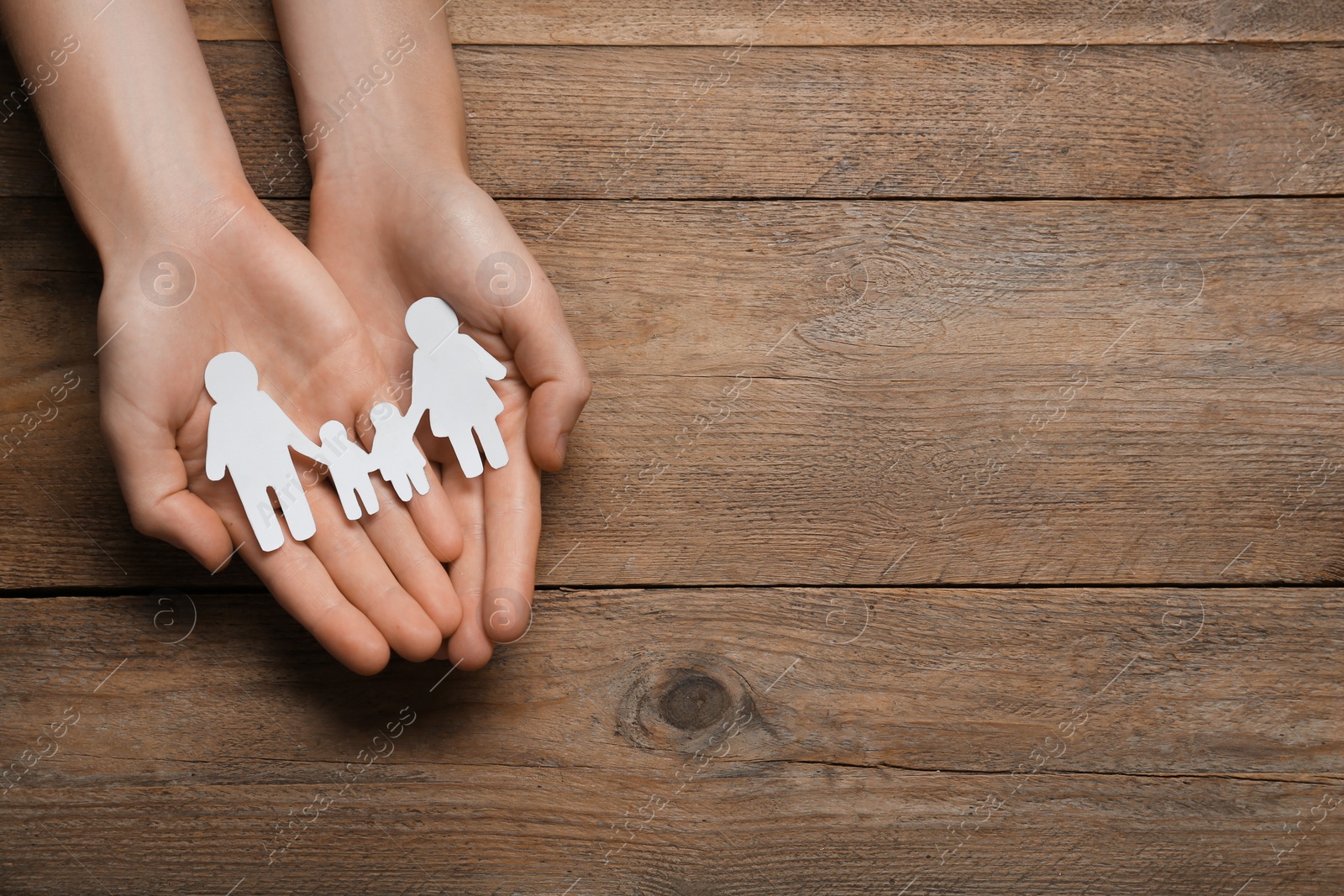 Photo of Woman holding paper family cutout at wooden table, top view. Space for text