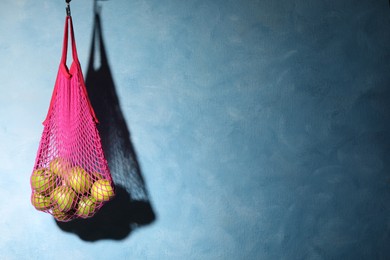 Photo of Mesh bag with ripe apples hanging on light blue background. Space for text