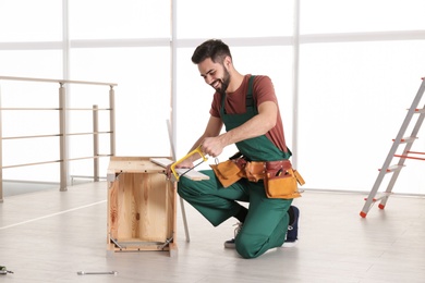 Carpenter in uniform making furniture indoors. Professional construction tools