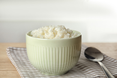 Photo of Bowl with tasty cooked rice on wooden table, closeup