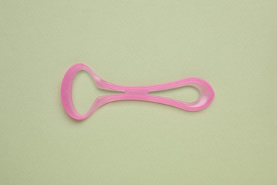 Photo of Pink tongue cleaner on olive background, top view