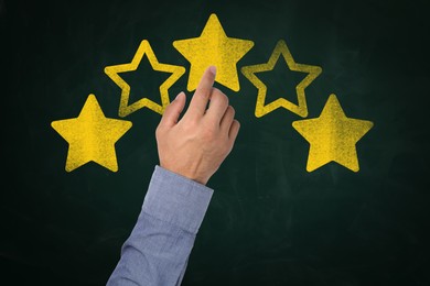 Image of Quality evaluation. Man touching golden star on green chalkboard, closeup