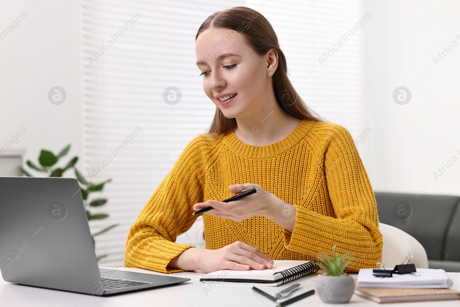 Photo of E-learning. Young woman using laptop during online lesson at white table indoors