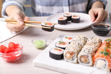 Photo of Woman taking tasty sushi roll with salmon from set at table, closeup