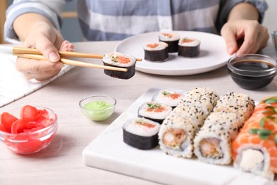 Woman taking tasty sushi roll with salmon from set at table, closeup