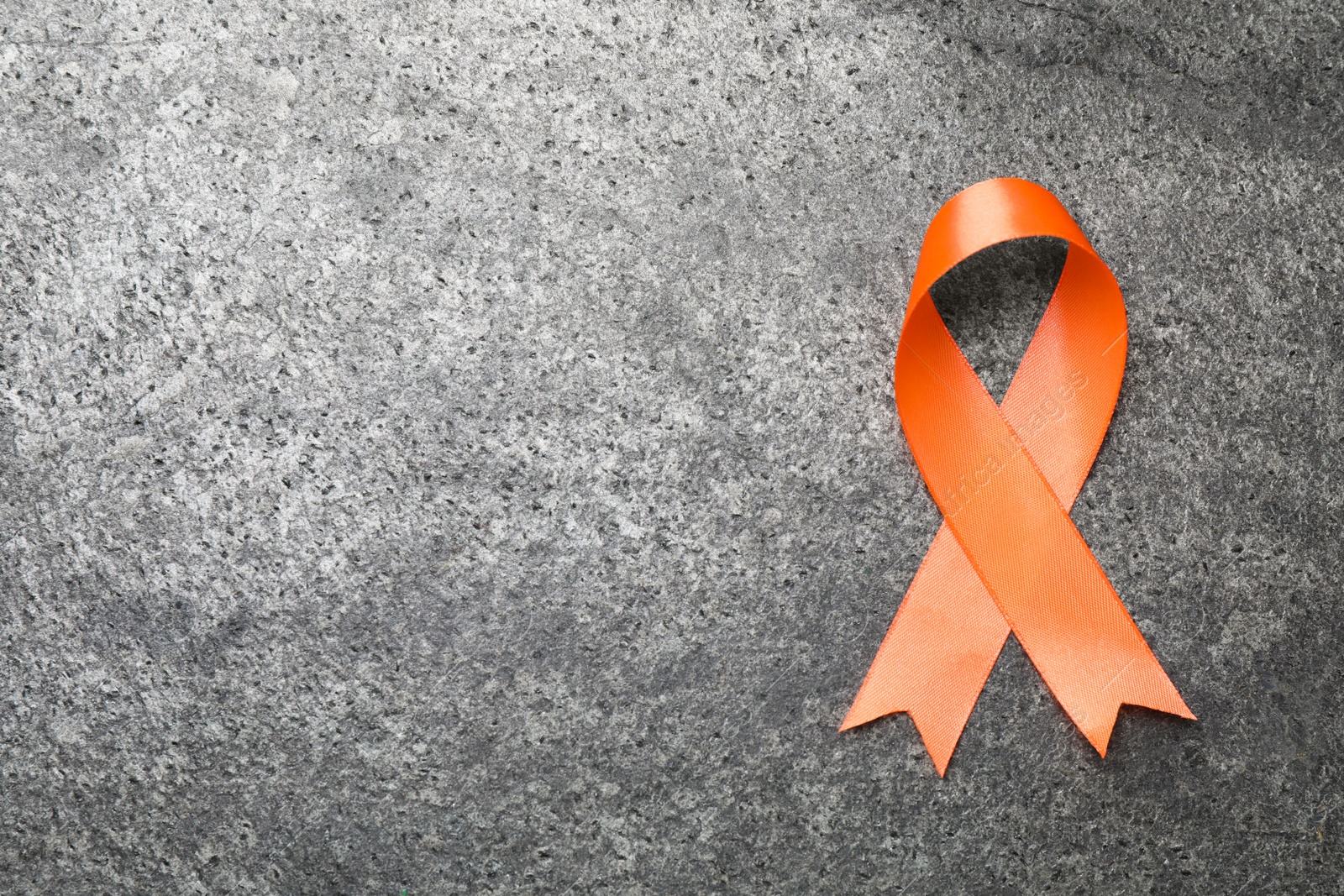 Photo of Orange ribbon on grey table, top view with space for text. Multiple sclerosis awareness