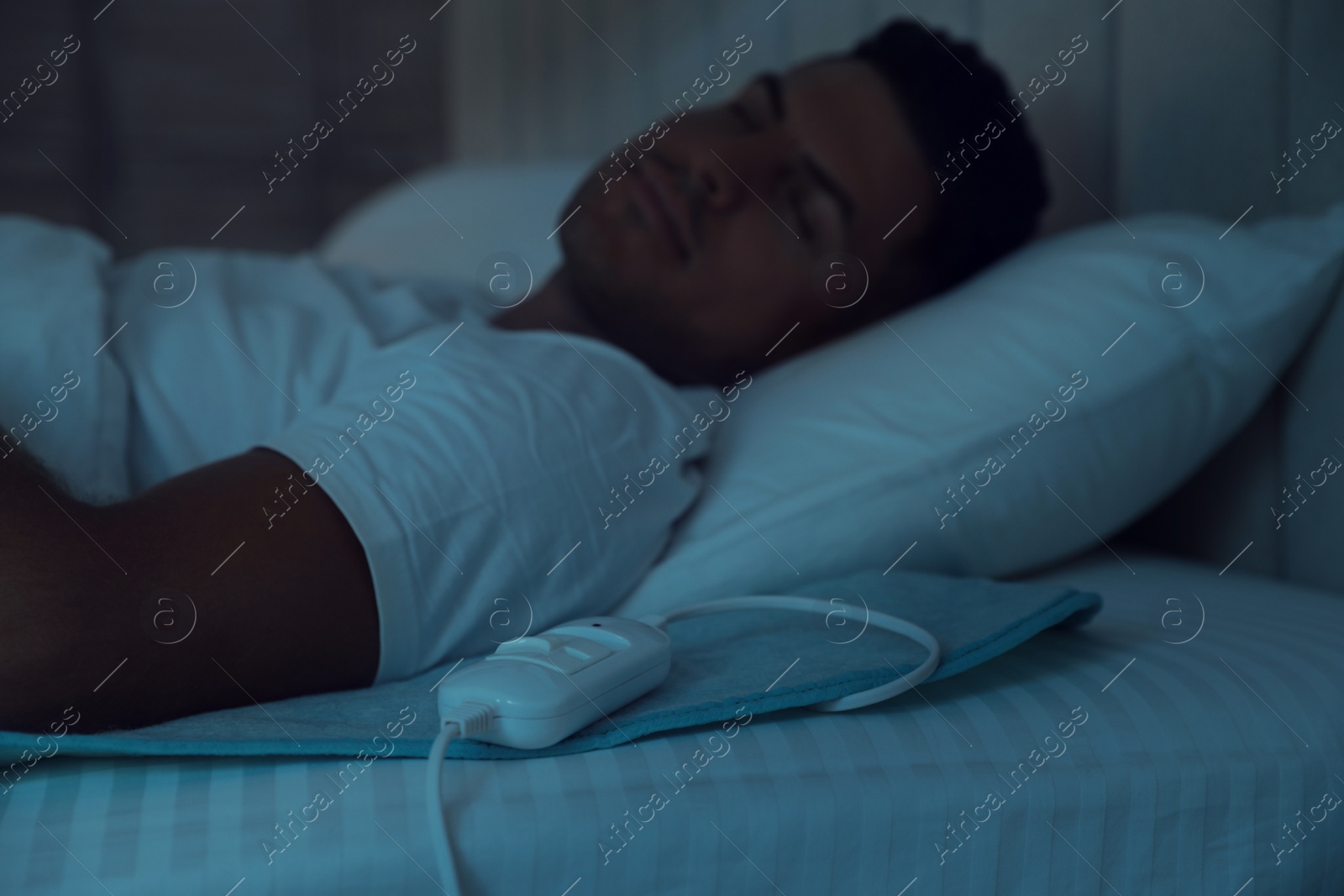 Photo of Man sleeping in bed with electric heating pad, focus on cable