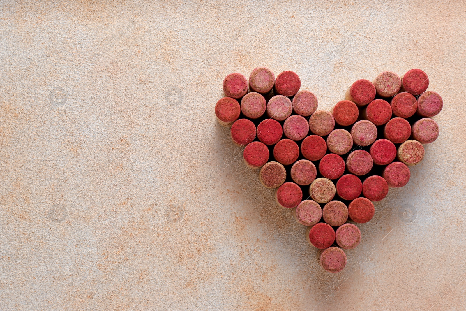 Photo of Heart made of wine bottle corks on textured table, top view. Space for text