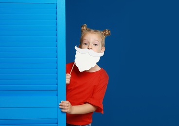 Cute little girl with Santa beard prop on blue background. Christmas celebration