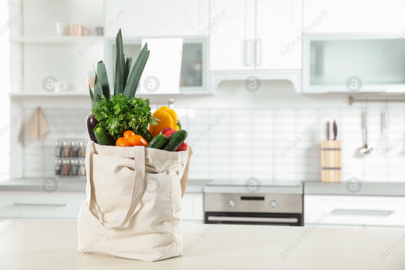 Photo of Textile shopping bag full of vegetables on table in kitchen. Space for text