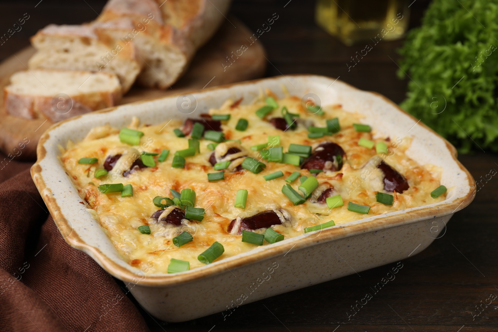 Photo of Tasty sausage casserole with green onions in baking dish on wooden table, closeup