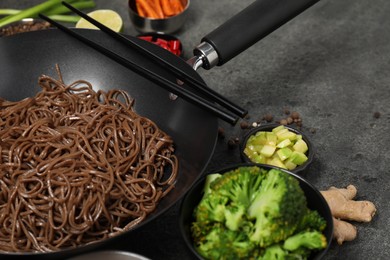 Wok with noodles and other products on grey table