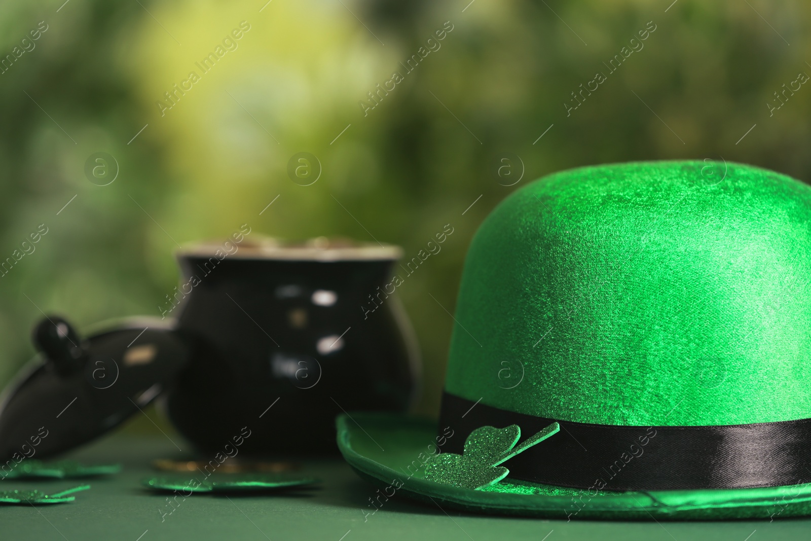 Photo of Leprechaun hat, clover leaves and pot of gold on table against blurred background, space for text. St Patrick's Day celebration