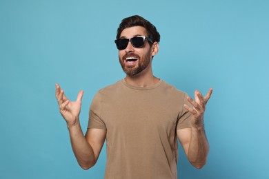 Photo of Portrait of excited bearded man with stylish sunglasses on light blue background