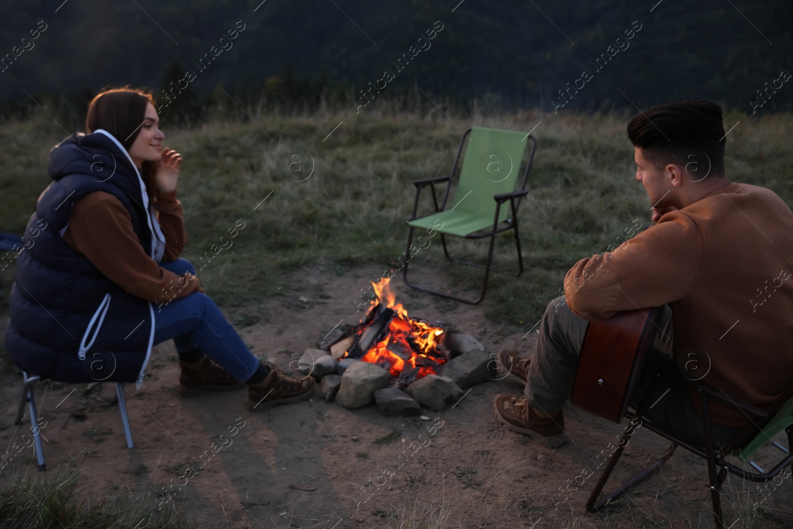 Photo of Couple with guitar sitting near bonfire at camping site