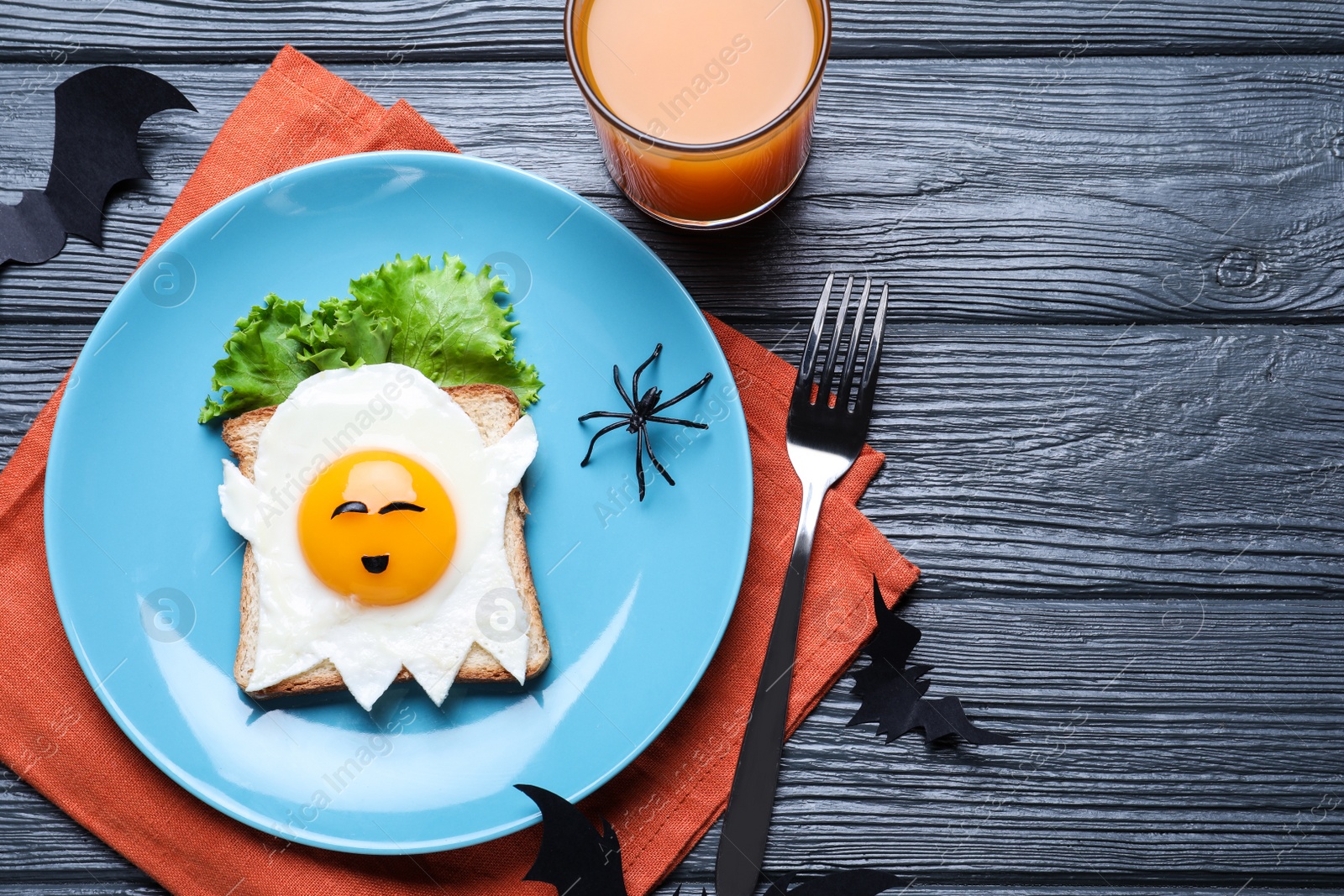 Photo of Halloween themed breakfast served on black wooden table, flat lay. Tasty toast with fried egg in shape of ghost