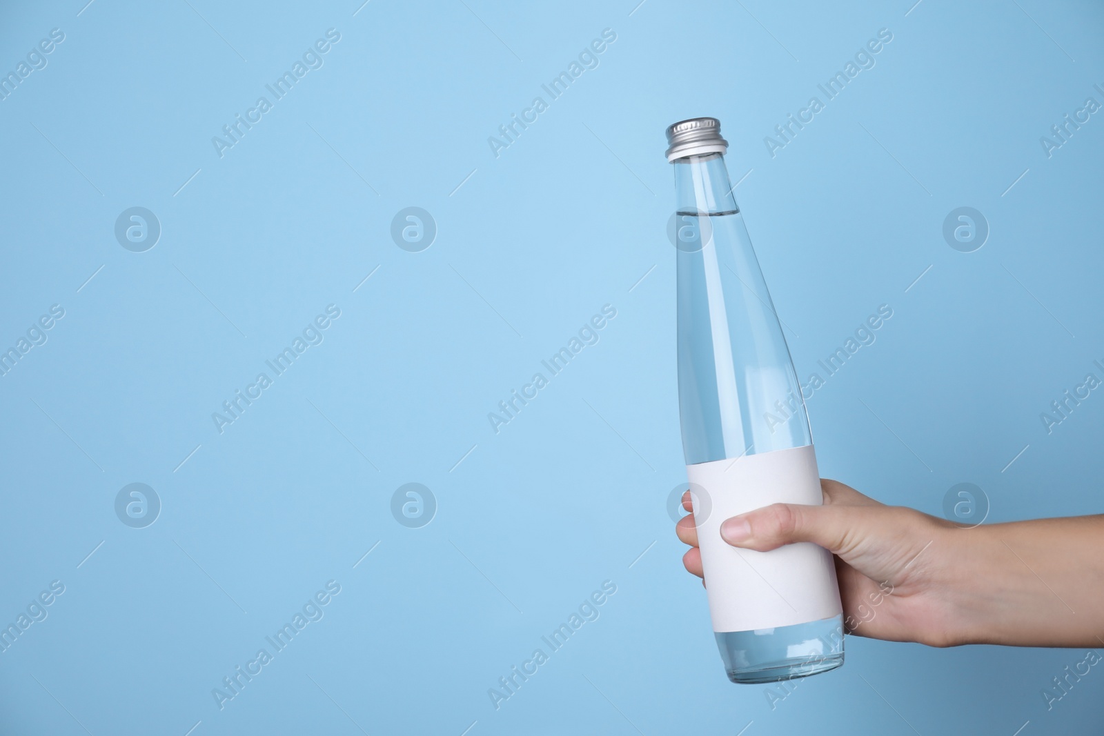 Photo of Woman holding glass bottle with soda water on light blue background, closeup. Space for text