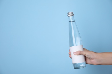 Woman holding glass bottle with soda water on light blue background, closeup. Space for text