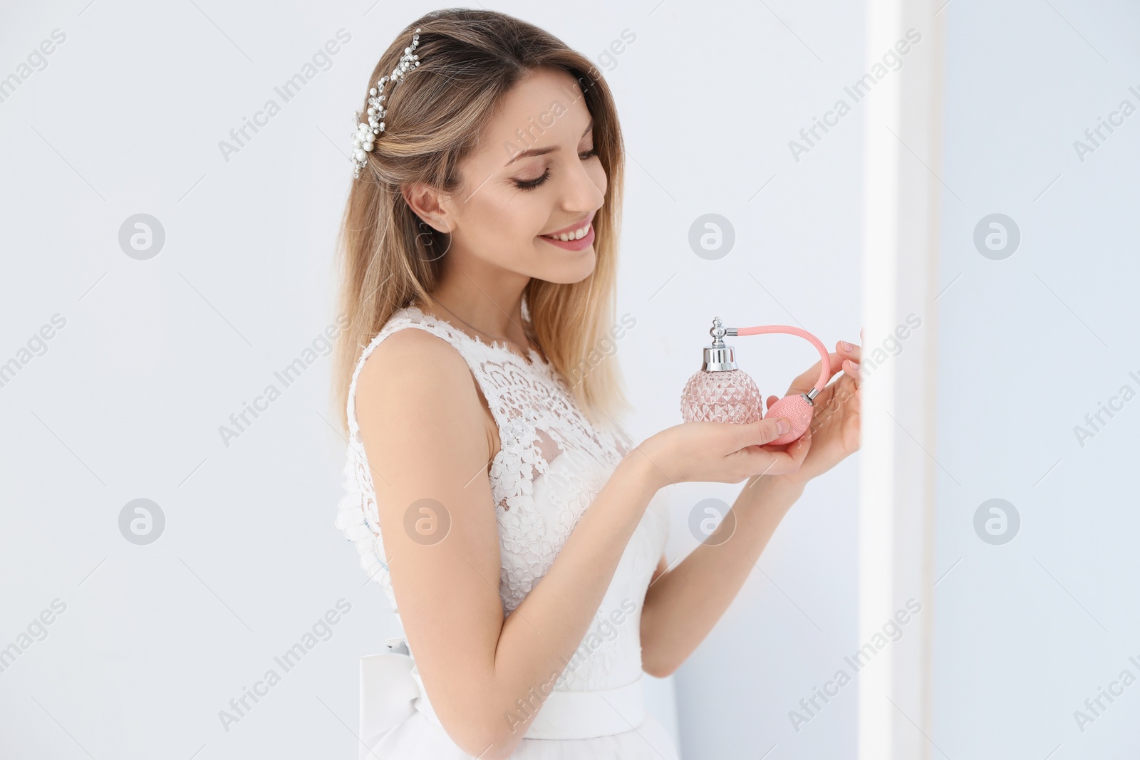 Photo of Beautiful young bride with bottle of perfume near mirror indoors