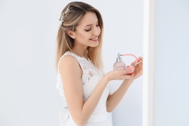 Beautiful young bride with bottle of perfume near mirror indoors