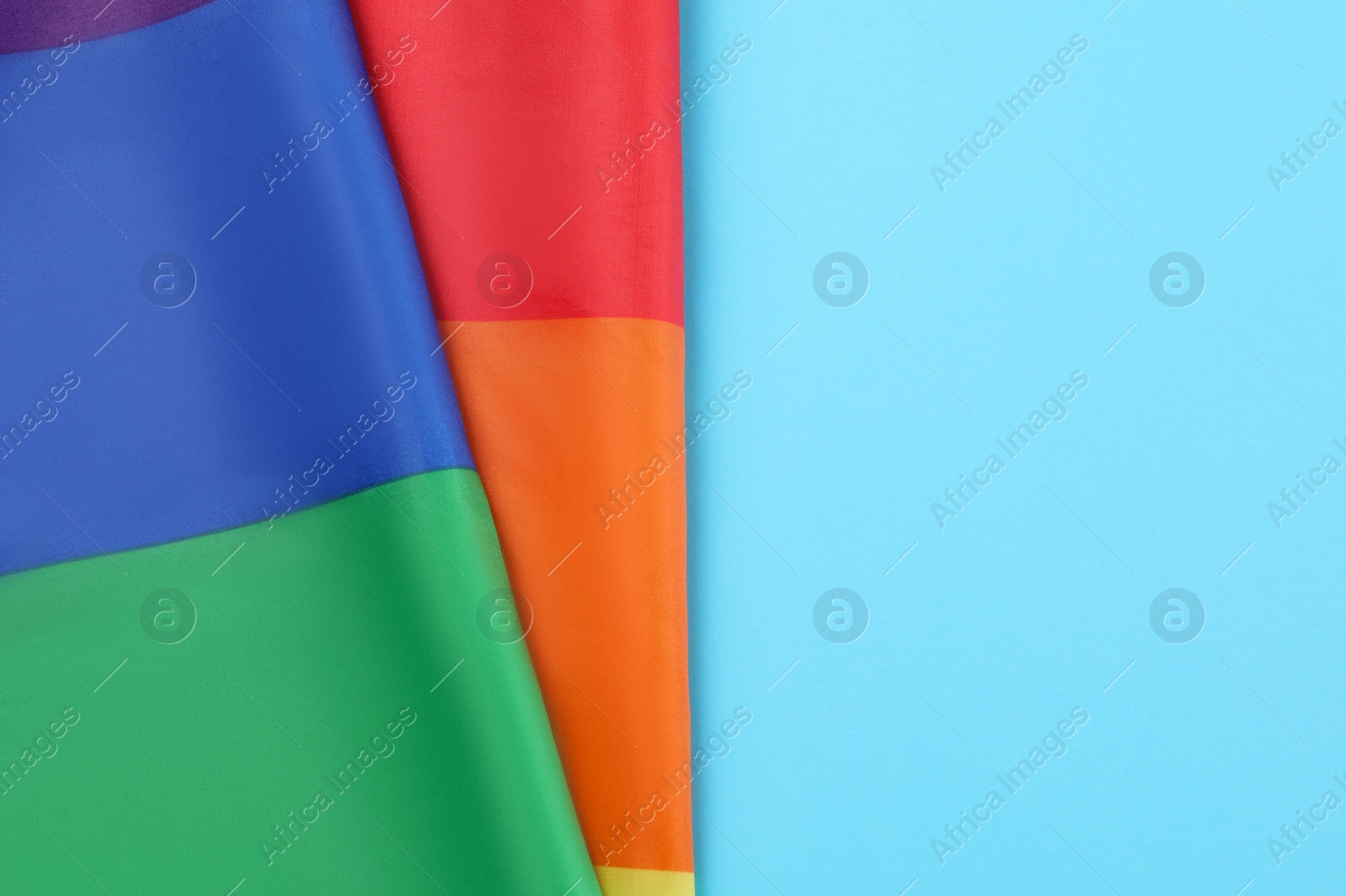 Photo of Rainbow LGBT flag on light blue background, top view. Space for text