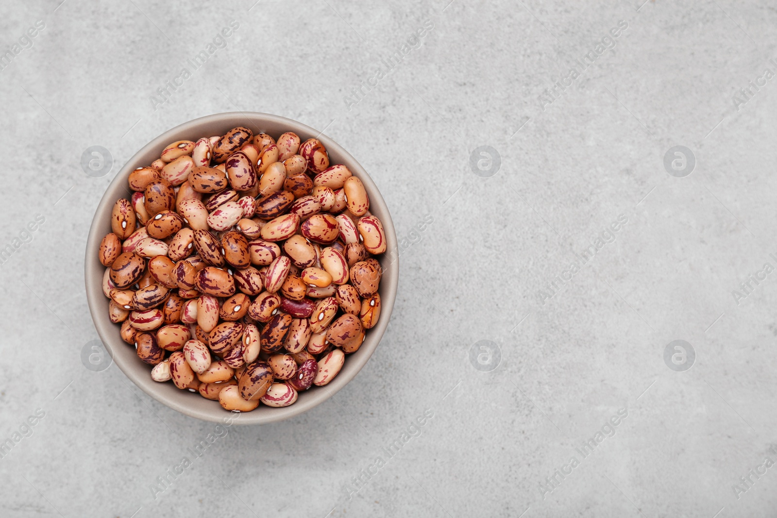 Photo of Bowl with dry kidney beans on light grey table, top view. Space for text