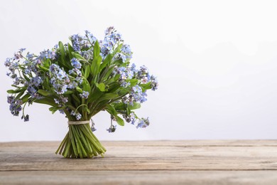 Bouquet of beautiful forget-me-not flowers on wooden table against white background, space for text