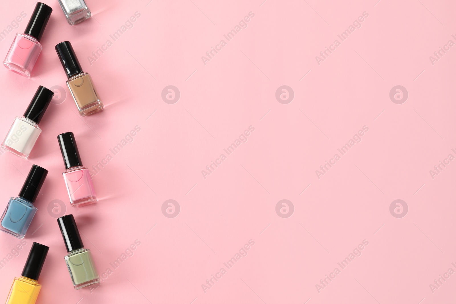 Photo of Pastel nail polishes in bottles on pink background, flat lay. Space for text
